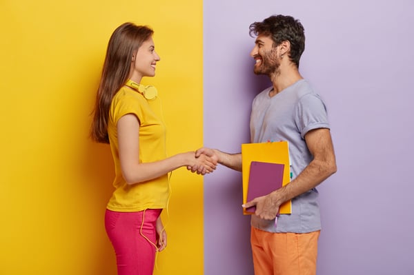 happy-groupmates-meet-after-holidays-shake-hands-agree-work-together-as-team-stand-profile-lovely-woman-with-headphones-meets-friend-unshaven-young-man-holds-notepad-talks-with-female